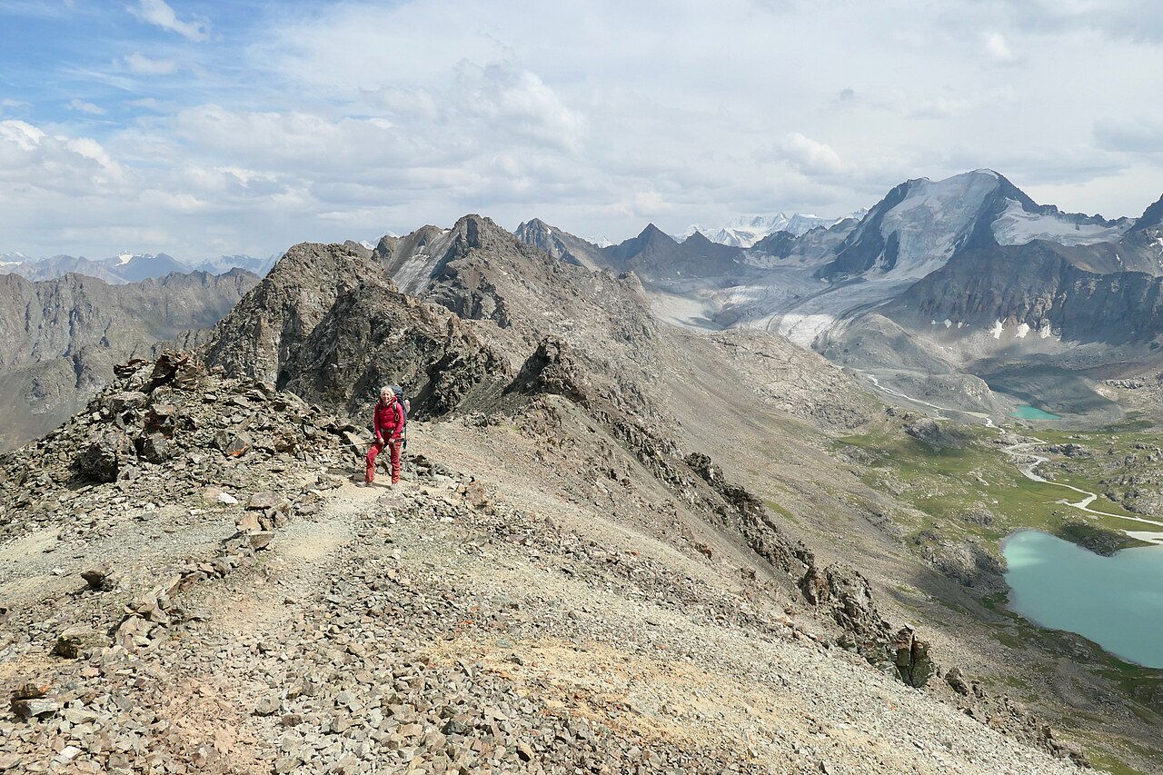 Trekker on a high ridge of the Ala-Kul trek with glacial lakes and peaks of the Terskey Alatau in Kyrgyzstan